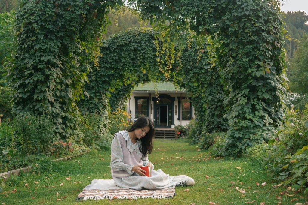 A young woman enjoys reading on a picnic blanket in a serene garden.