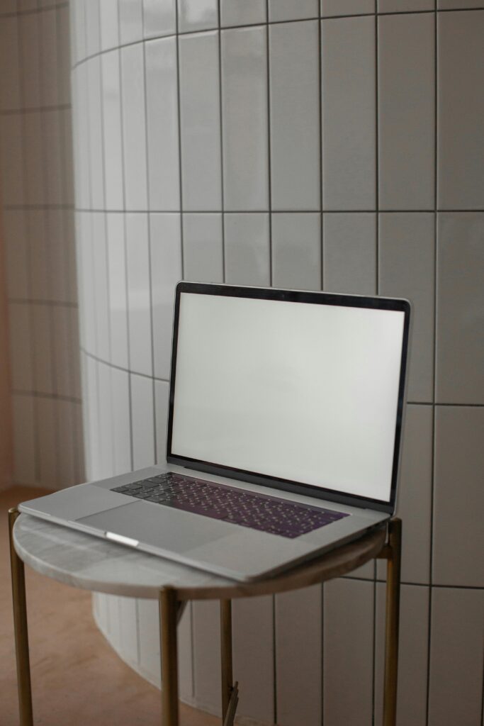 A sleek laptop with a blank screen on a round side table against a modern tile wall, ideal for design mockups.