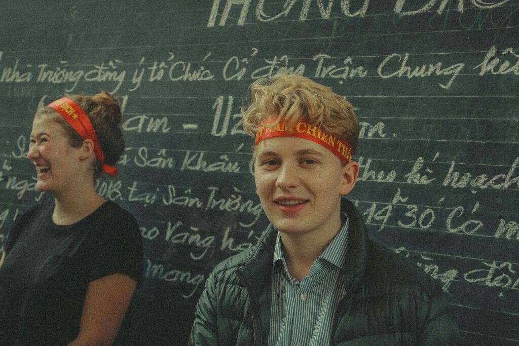Two young adults smiling in front of a Vietnamese chalkboard.