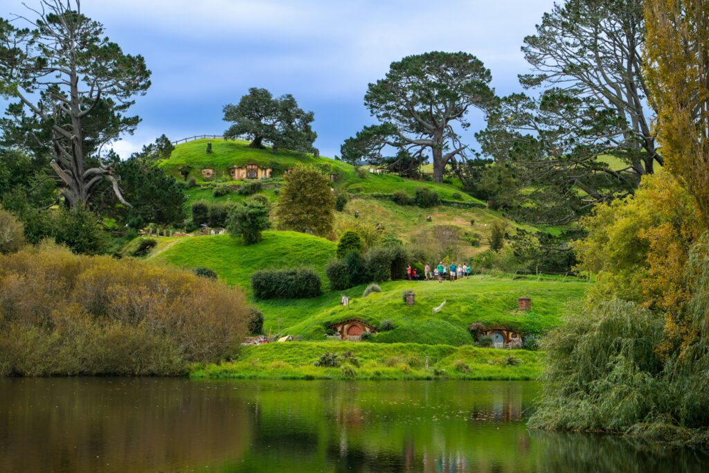 Lush green landscape of Hobbiton with iconic hobbit holes and serene lake reflecting the vibrant scenery.