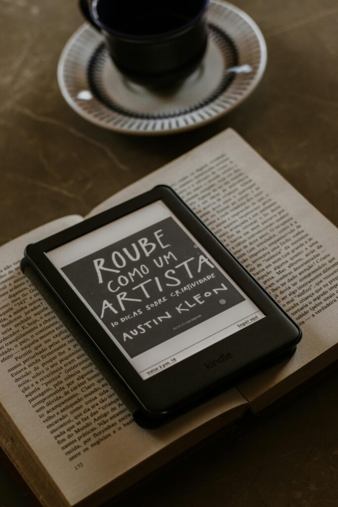 An e-reader displaying a book cover placed on an open book next to a coffee cup.