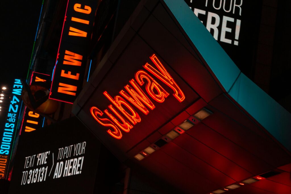 Bright neon 'Subway' sign illuminated at night in Times Square, New York City.