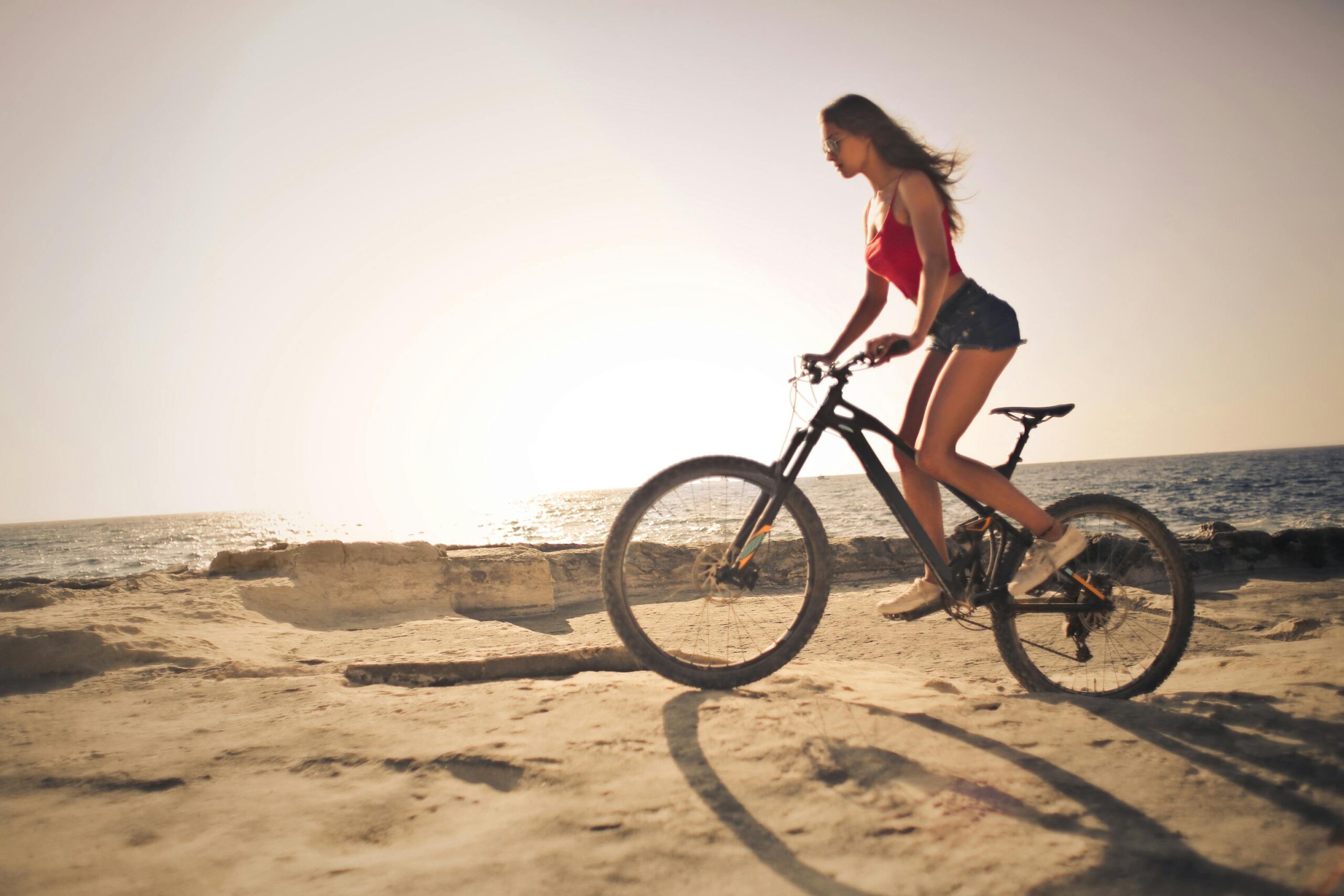 A woman rides a bicycle along the sandy shores with a scenic sea view during sunset in Malta.