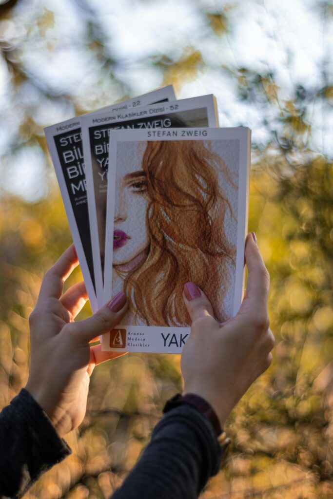 Hands holding Stefan Zweig books with blurred autumn foliage background.