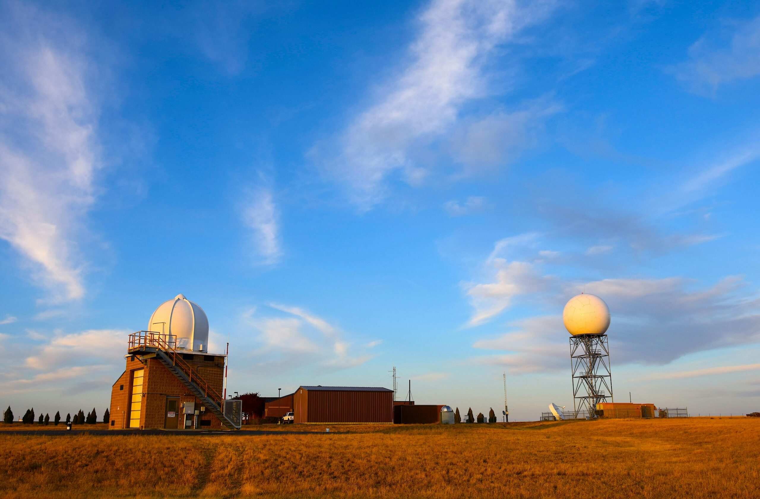 Weather radar station set in a field with a clear blue sky and scattered clouds, showcasing meteorological technology.