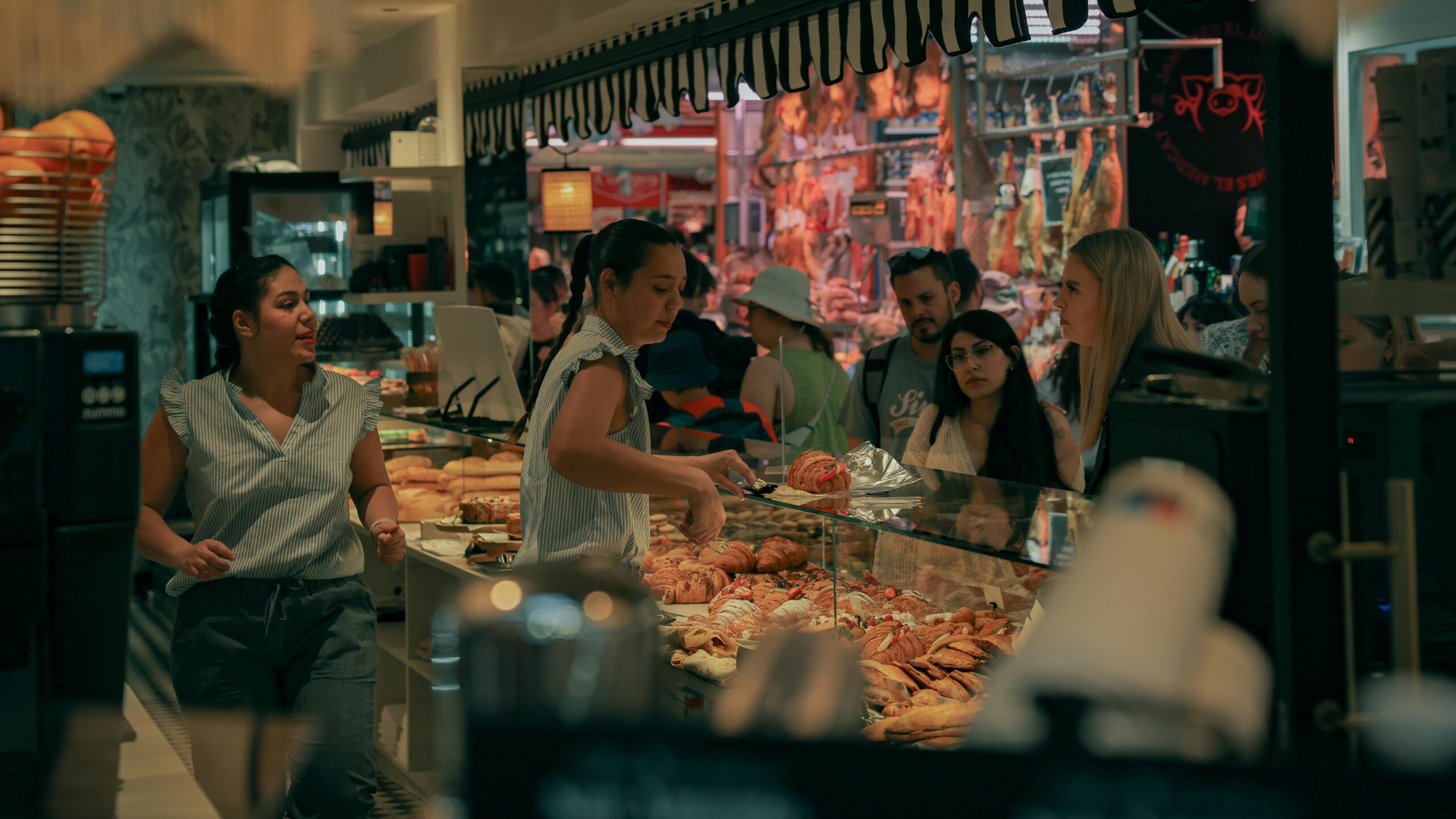 Lively indoor bakery scene in Valencia's bustling market with diverse customers and baked goods.