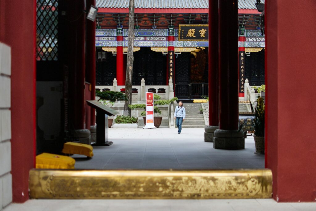 A lone man walks inside a beautifully ornate Chinese temple entrance, showcasing traditional architecture.