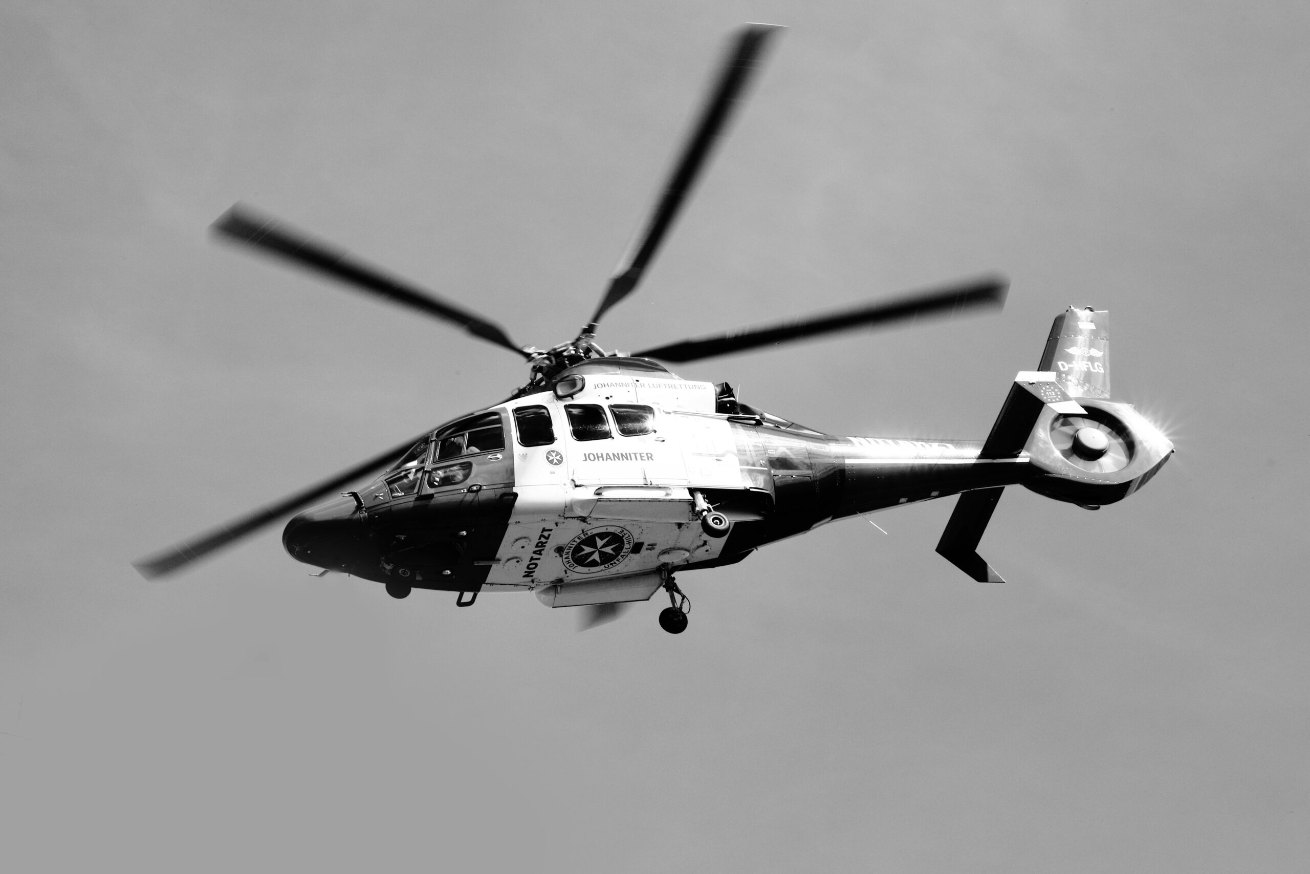 A black and white image of a helicopter soaring in the sky, with blurred rotors in motion.