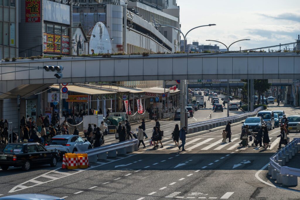 Dynamic urban street scene with pedestrians crossing, cars, and bustling activity under a walkway.