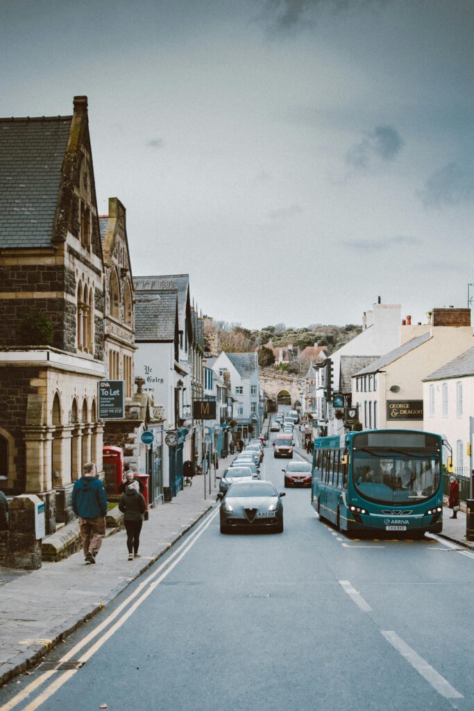 A bustling street in Conwy, Wales with cars, bus, and pedestrians on a cloudy winter day.