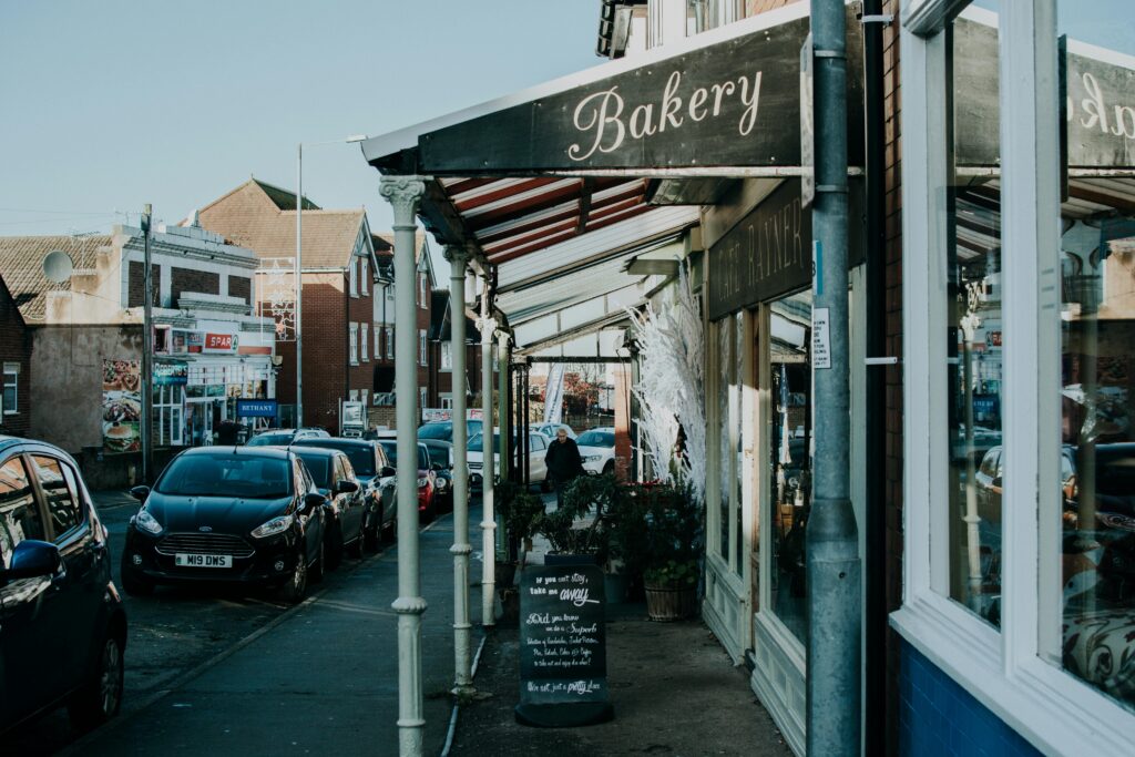 A bustling street with a bakery and parked cars under clear daylight.