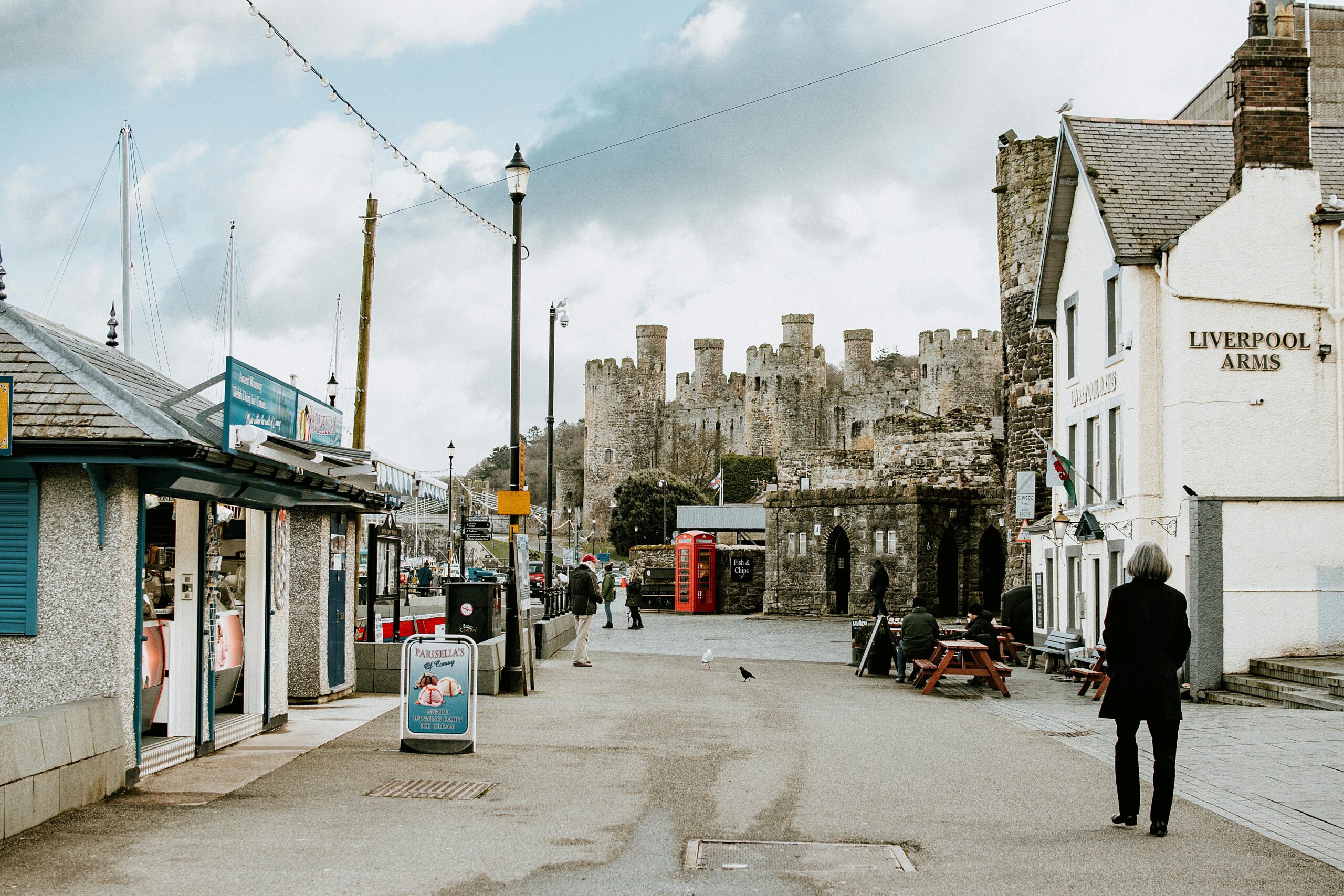 Street scene with Conwy Castle, shops, and pedestrians in Wales, UK.