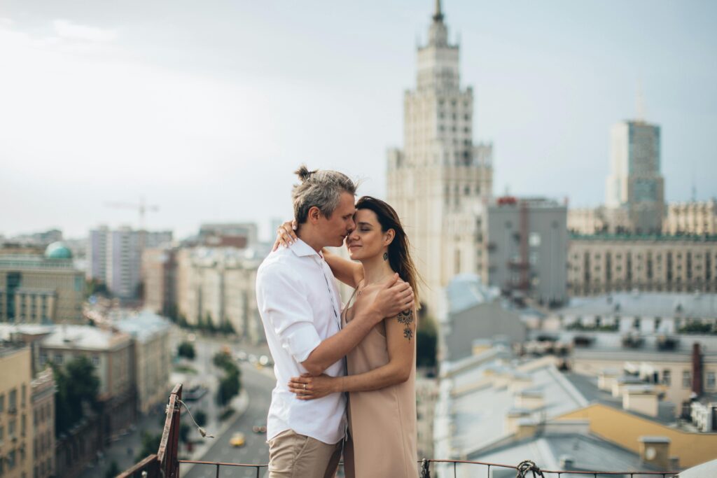 A couple shares an intimate moment atop a rooftop with a scenic view of Moscow's skyline.