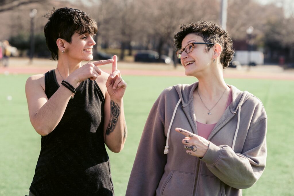 Two women sharing a joyful moment outdoors, pointing at each other playfully.