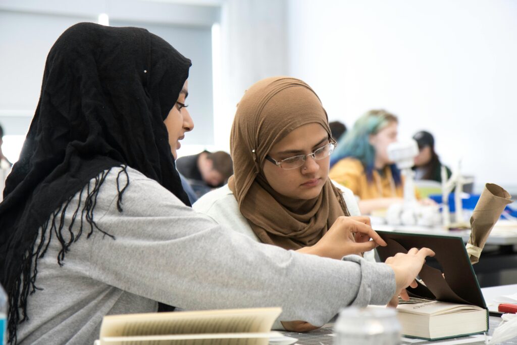Two female college students collaborating on a project in a modern classroom setting.