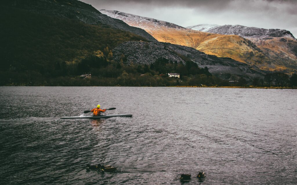 Solo kayaker paddles on a scenic lake with Welsh mountains, ideal for adventure seekers.