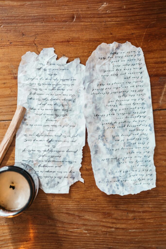 Two burnt manuscripts beside a lit candle on a rustic wooden table, evoking a vintage and moody ambiance.