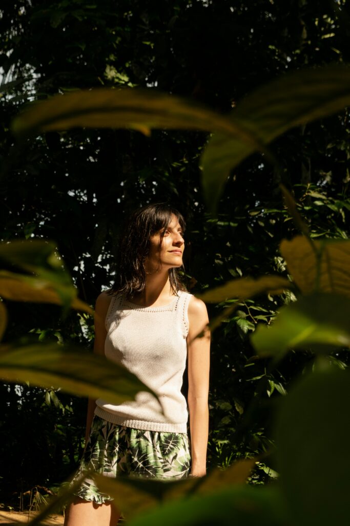 Woman in jungle basking in sunlight wearing tropical attire amidst lush foliage.