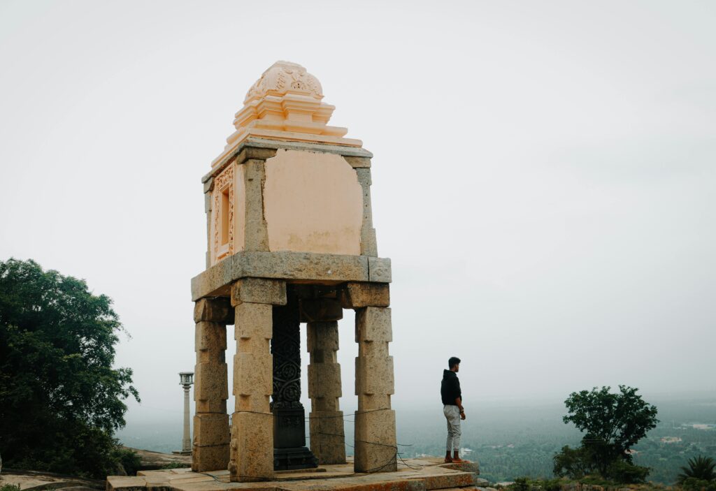 A man stands beside a historic stone pavilion on a foggy day, evoking a sense of solitude.