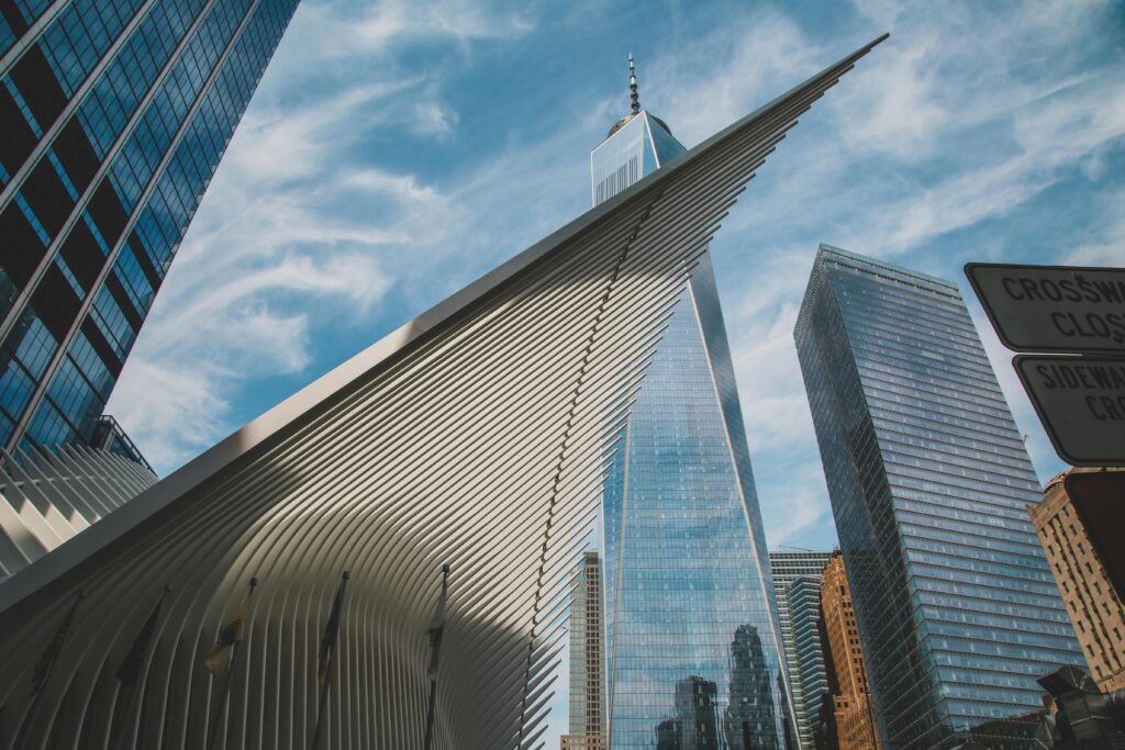 Dramatic angle of New York City's One World Trade Center and surrounding skyscrapers against a blue sky.