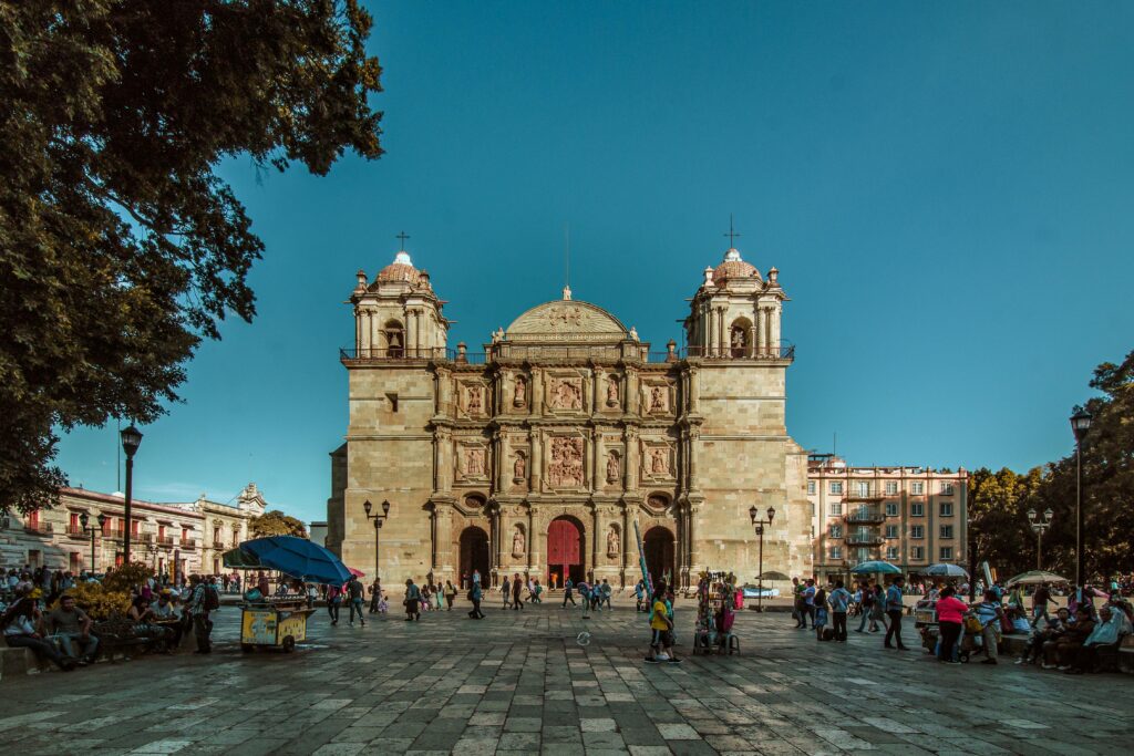 Scenic view of Oaxaca Cathedral with vibrant town square and visitors under a clear blue sky.