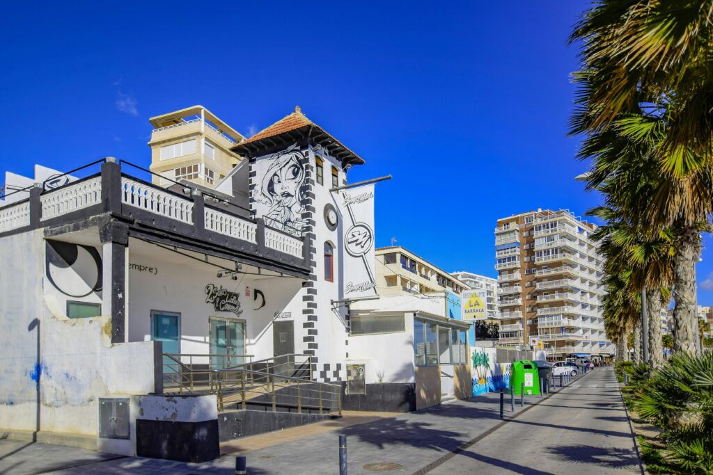 Street scene featuring a mural and palm trees in Villajoyosa, Spain under a clear blue sky.