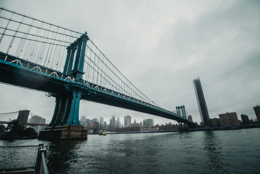 View of Manhattan Bridge with city skyline in the background on a cloudy day.