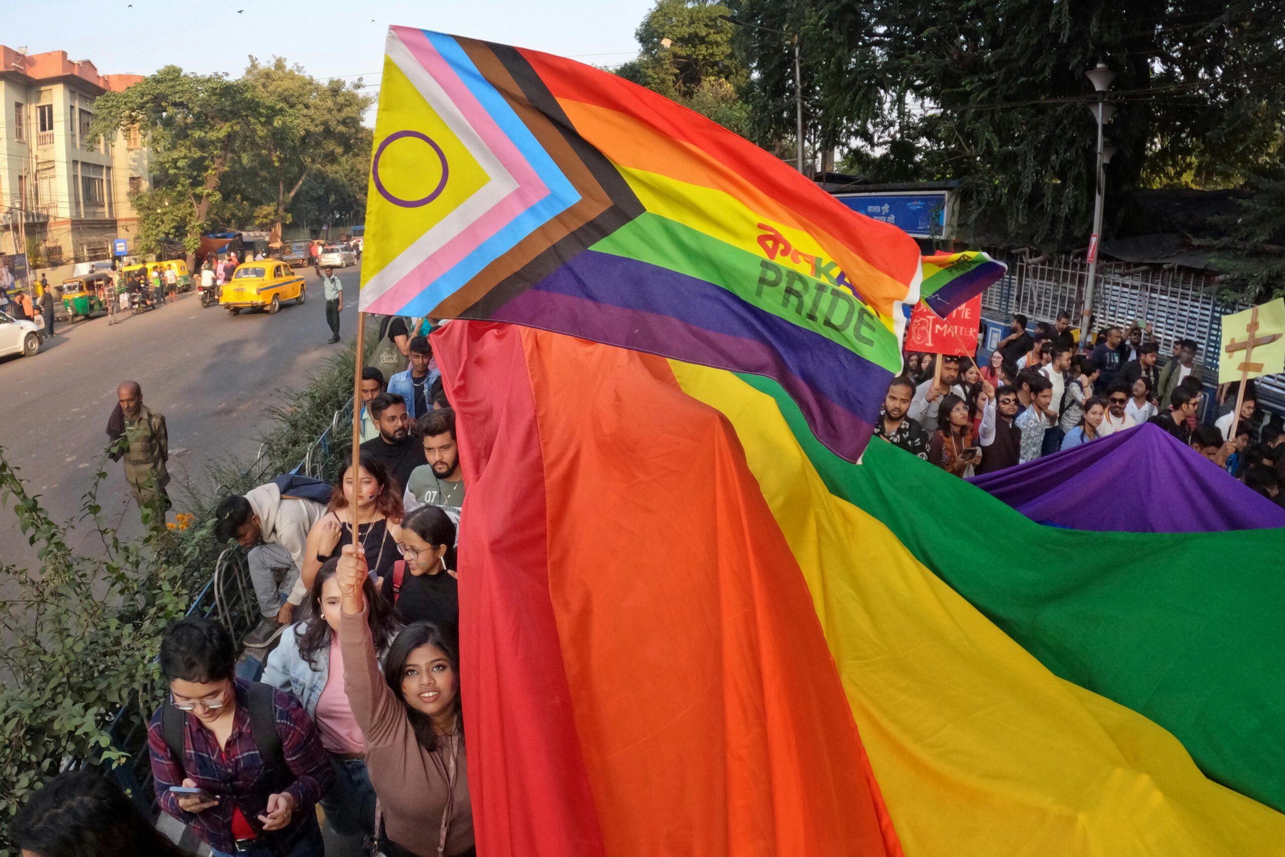 Vibrant LGBTQ+ pride parade in Kolkata, India with participants and colorful flags.