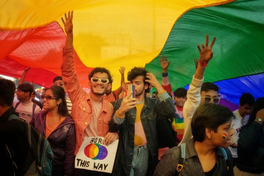 Joyful crowd under a rainbow flag celebrating Pride in Kolkata, India.