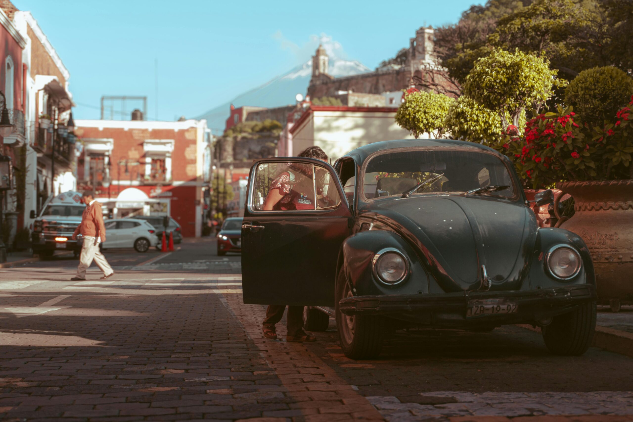 Classic car parked on a charming street in Atlixco, Mexico with scenic backdrop.