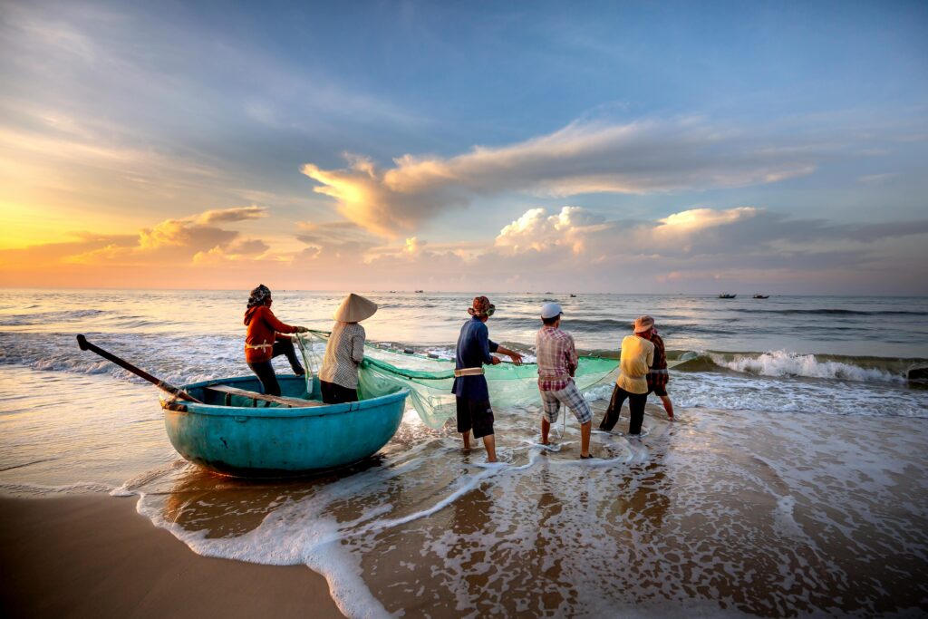 Fishermen haul in nets on a sandy beach, bathed in warm sunrise hues.