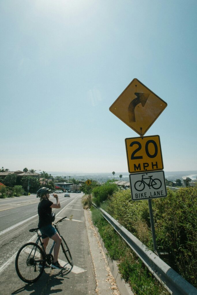 Cyclist pauses near bike lane sign on a sunny road for a drink.