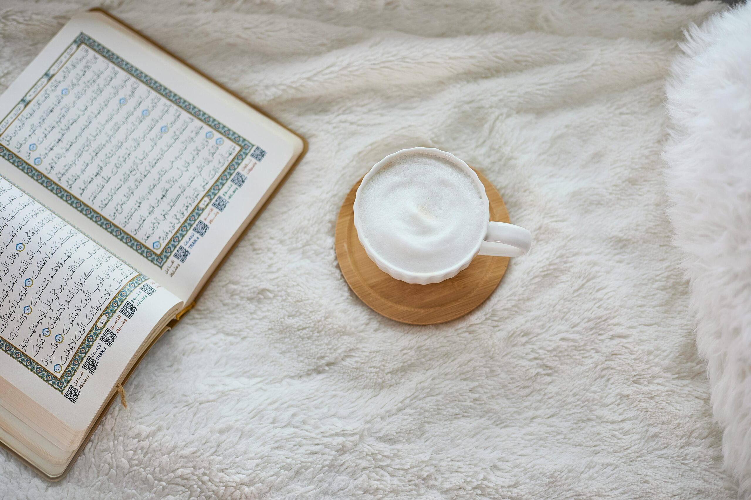 A cozy setup featuring an open Quran and a cup of coffee on a fluffy surface.