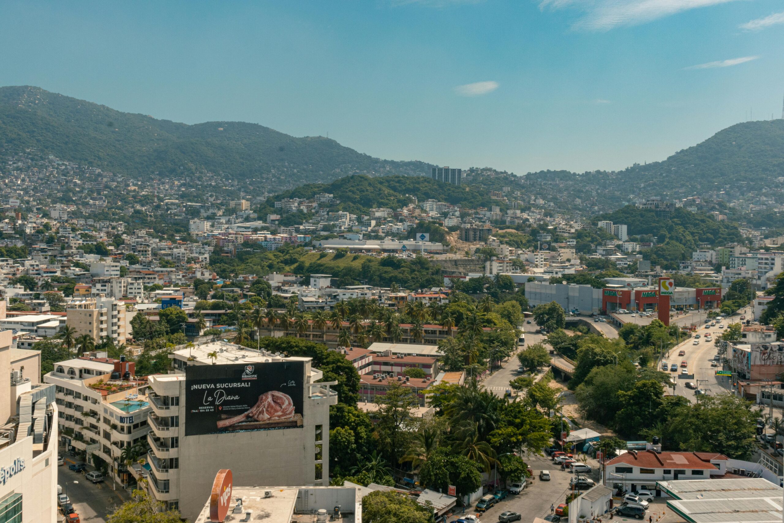 A breathtaking aerial view of Acapulco with lush hills and urban landscape under a clear blue sky.