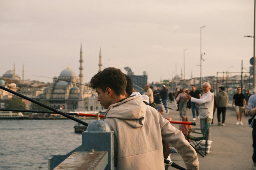 People fishing on Galata Bridge with a view of Istanbul's iconic skyline during the day.