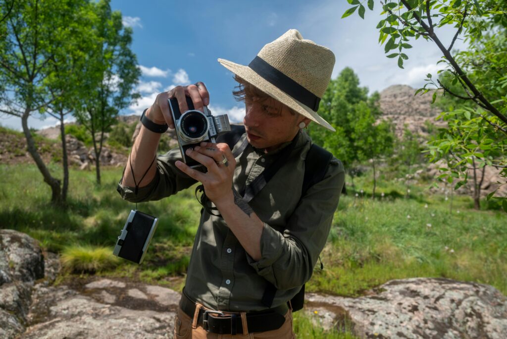 Photographer using a vintage camera outdoors at Manzanares el Real, Spain, surrounded by vibrant summer landscape.