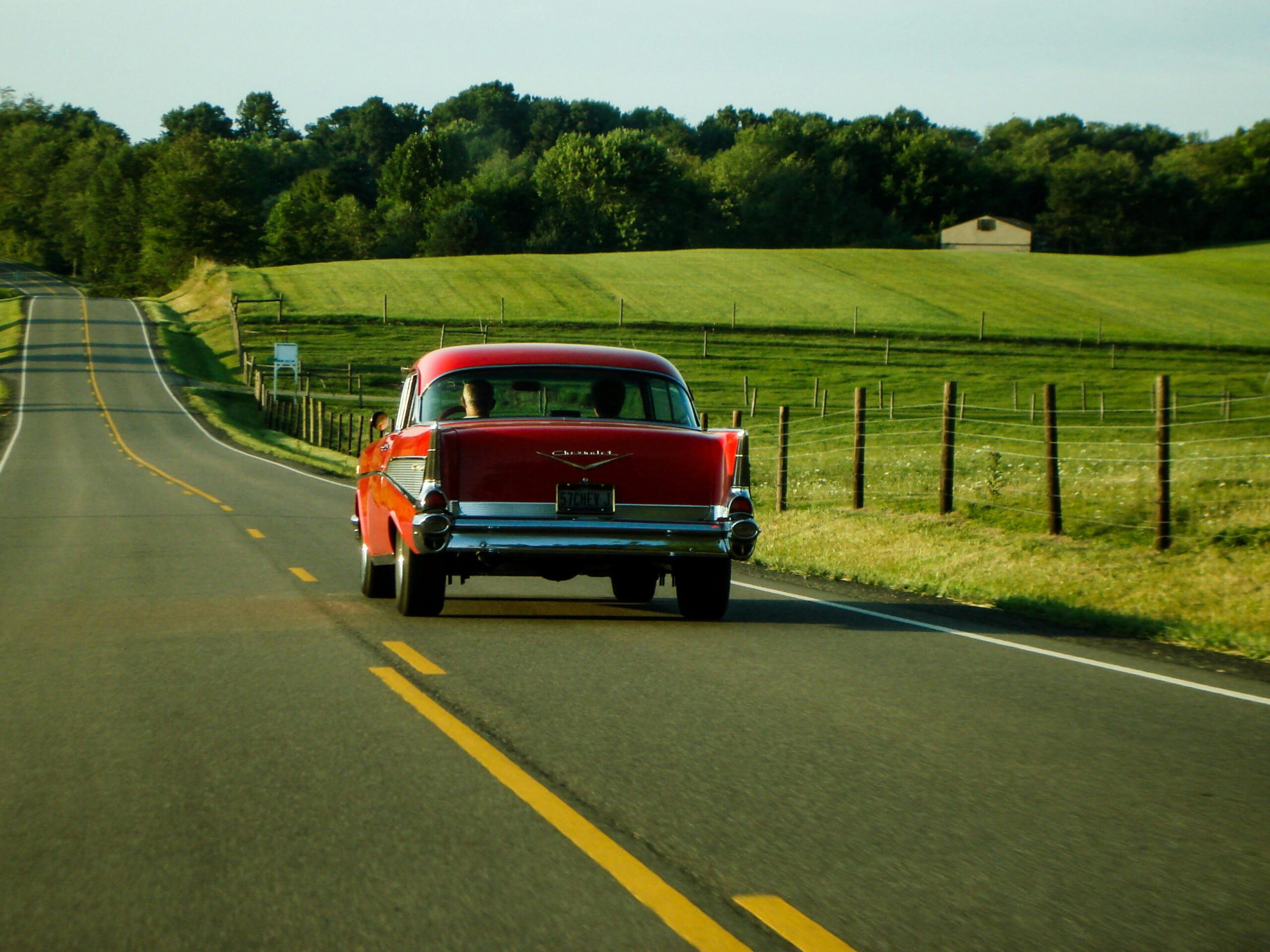 Classic red car driving on a scenic countryside road in Ohio, capturing a vintage travel vibe.