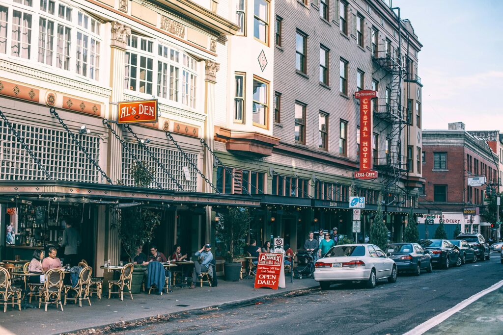 Vibrant street view featuring outdoor seating at a café and multiple parked cars on a sunny day.