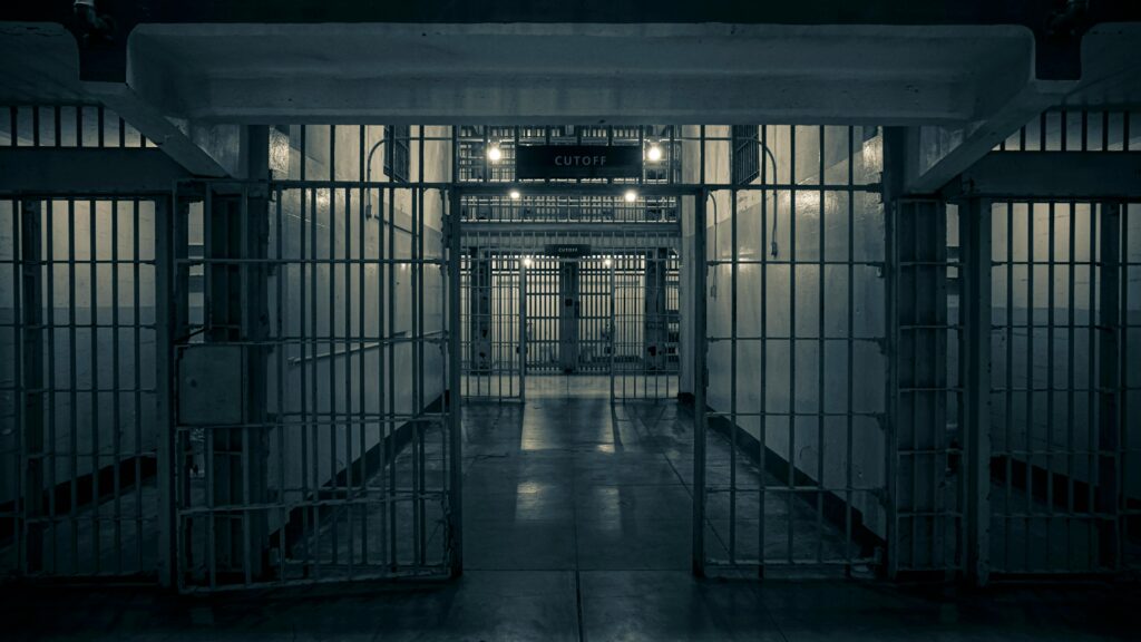 Moody interior of a prison corridor with metal bars, evoking a sense of confinement.