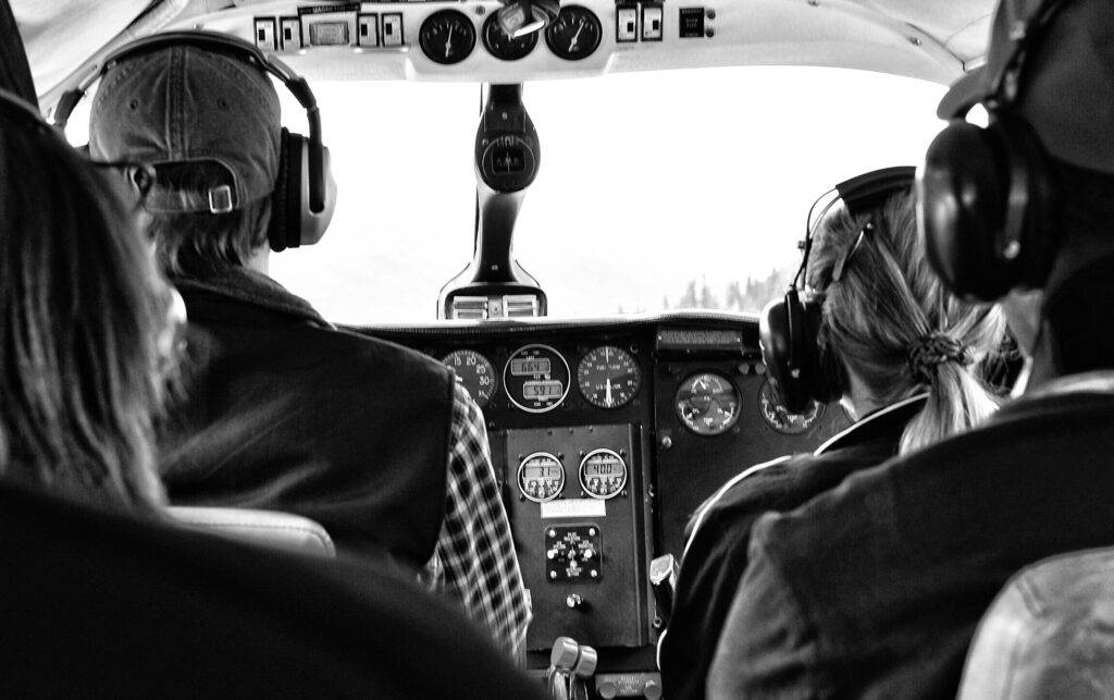 Black and white image of pilots in a small aircraft cockpit, emphasizing teamwork and aviation.