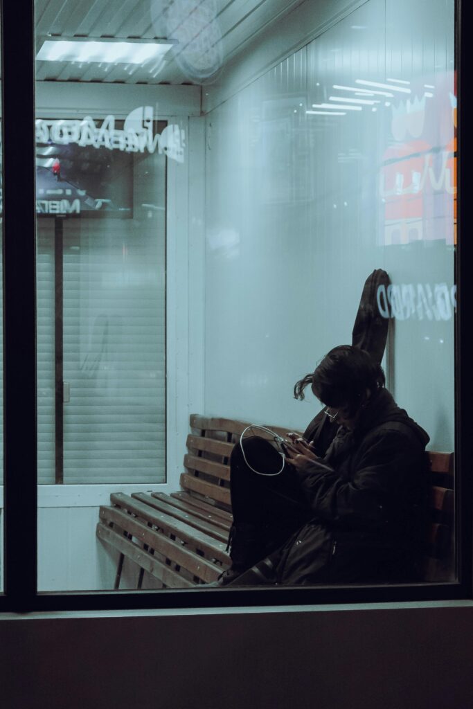A woman sits alone on a bench inside an airport terminal, checking her phone.