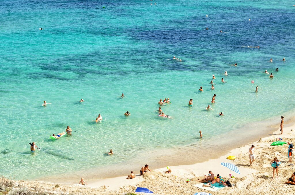 People enjoying a sunny day at a beautiful beach in Mallorca, Spain, with turquoise water and sandy shores.