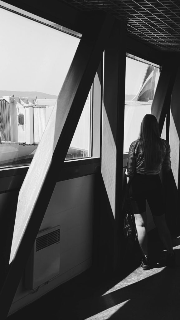 Black and white photo of a woman viewing an airport runway through large windows.