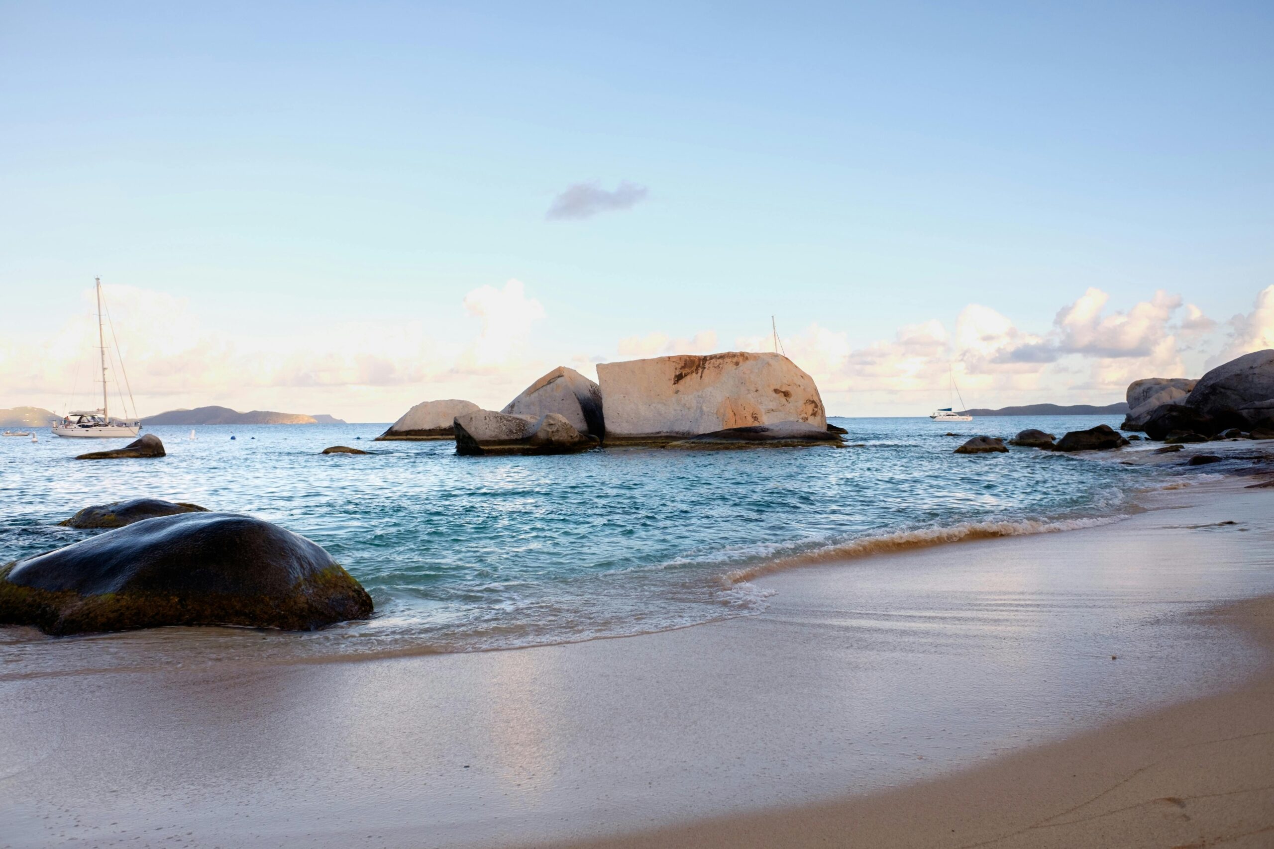 Serene coastal view with rocks, sandy beach, and boats at sunset.