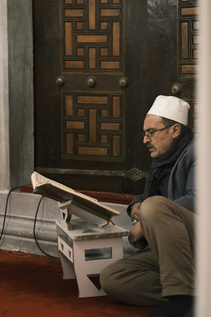 A man sits on the floor of a mosque, reading a book, conveying a serene and introspective moment.