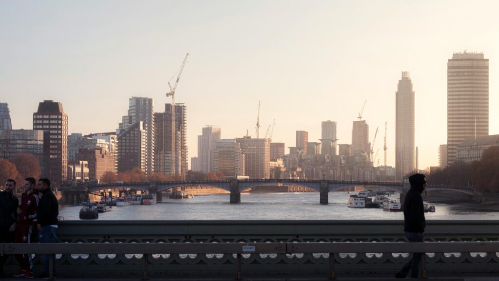 Skyline of London at twilight with the River Thames, bridge, and silhouettes of people.