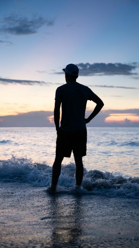 A man in silhouette stands on Myrtle Beach, SC, watching the ocean waves at sunset.