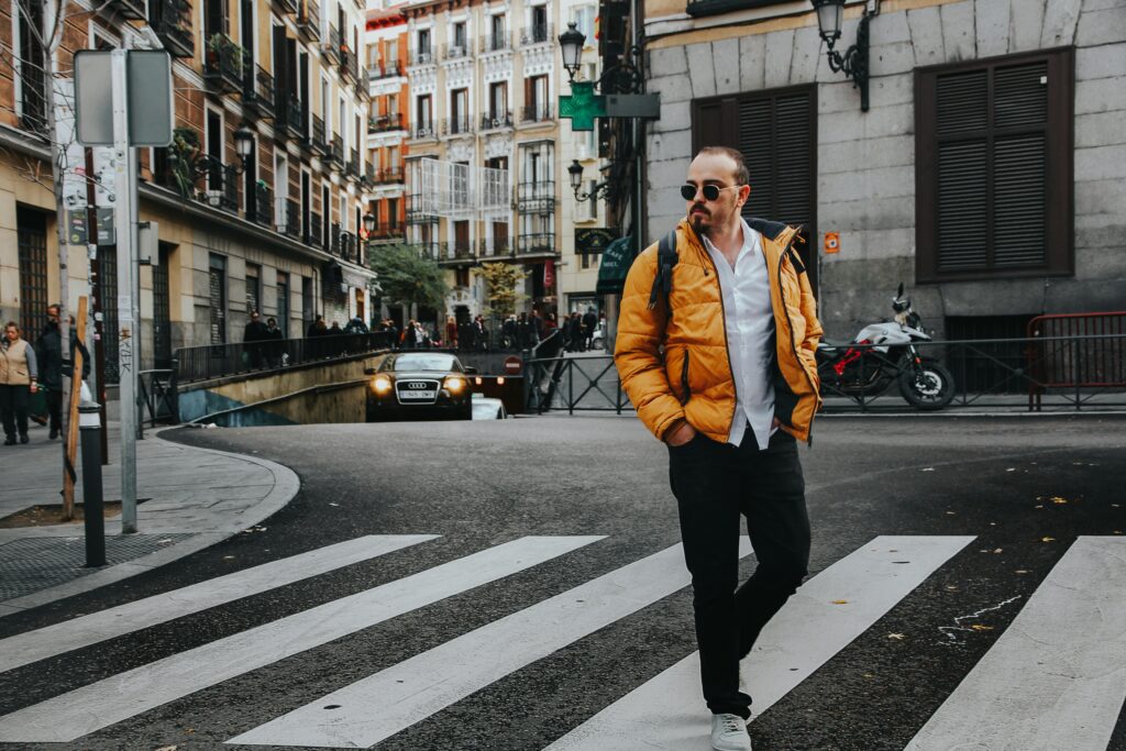 A fashionable man crosses a street in Madrid, showcasing urban style and city life.