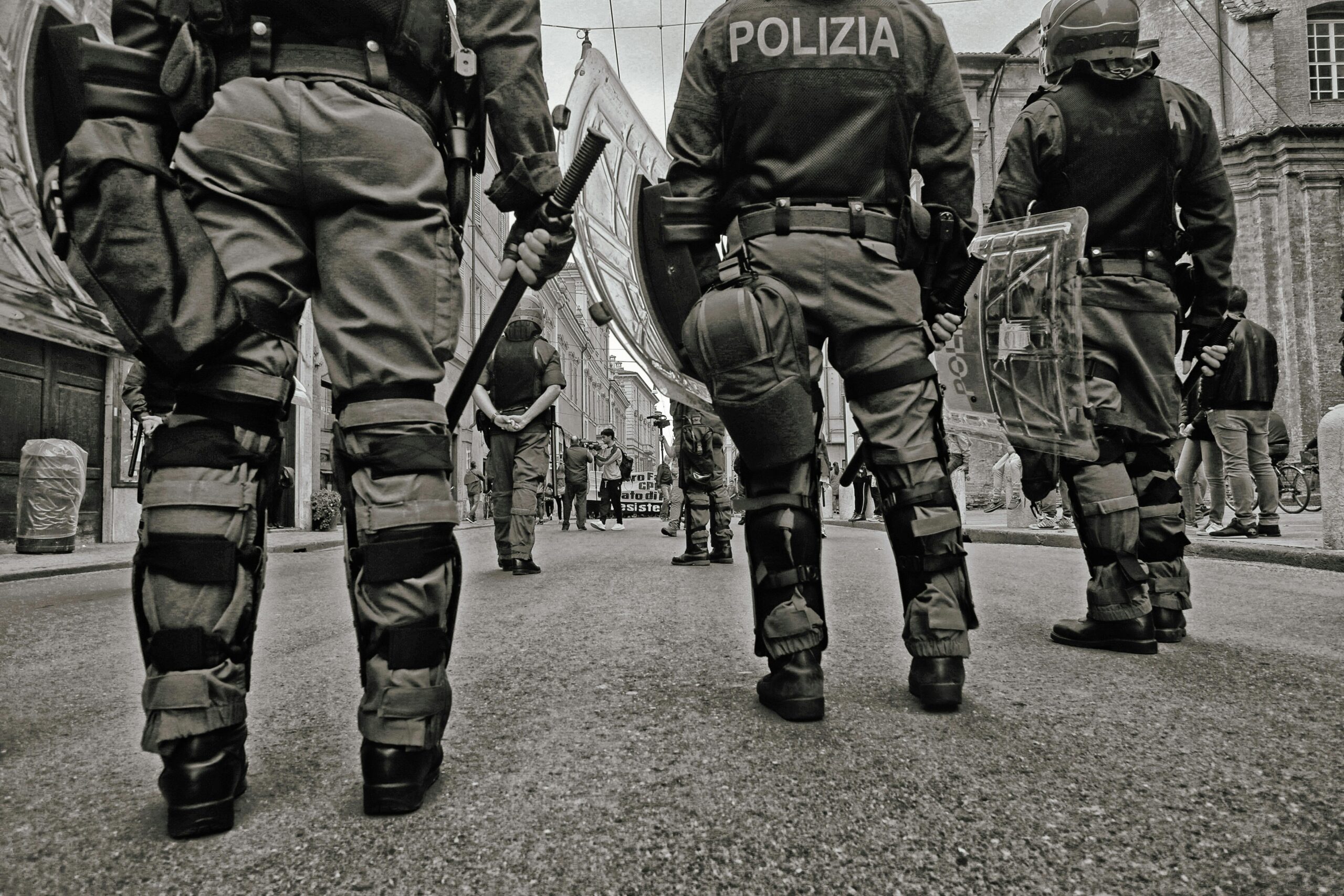 Black and white image of police officers with tactical gear during street patrol in an urban setting.