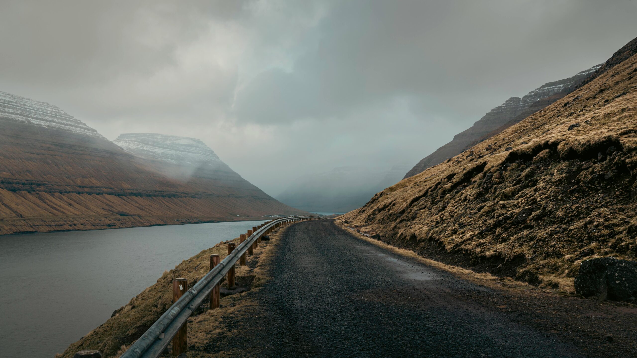Dramatic road view in the Faroe Islands with misty mountains and a cloudy sky.